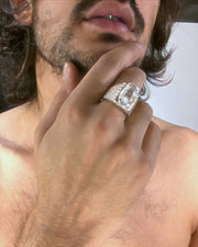 A scale textured silver ring holding a large faceted quartz crystal that revolves on its axis.  